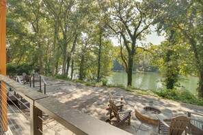 A patio area with Adirondack chairs, a fire pit, and a view of a lake surrounded by trees. - Riverfront Salesville Cabin Rental w/ Shared Dock! (Mountain Home)