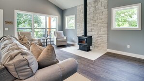 A living room with a stone fireplace, large windows, and a gray couch. - Riverfront Salesville Cabin Rental w/ Shared Dock! (Mountain Home)