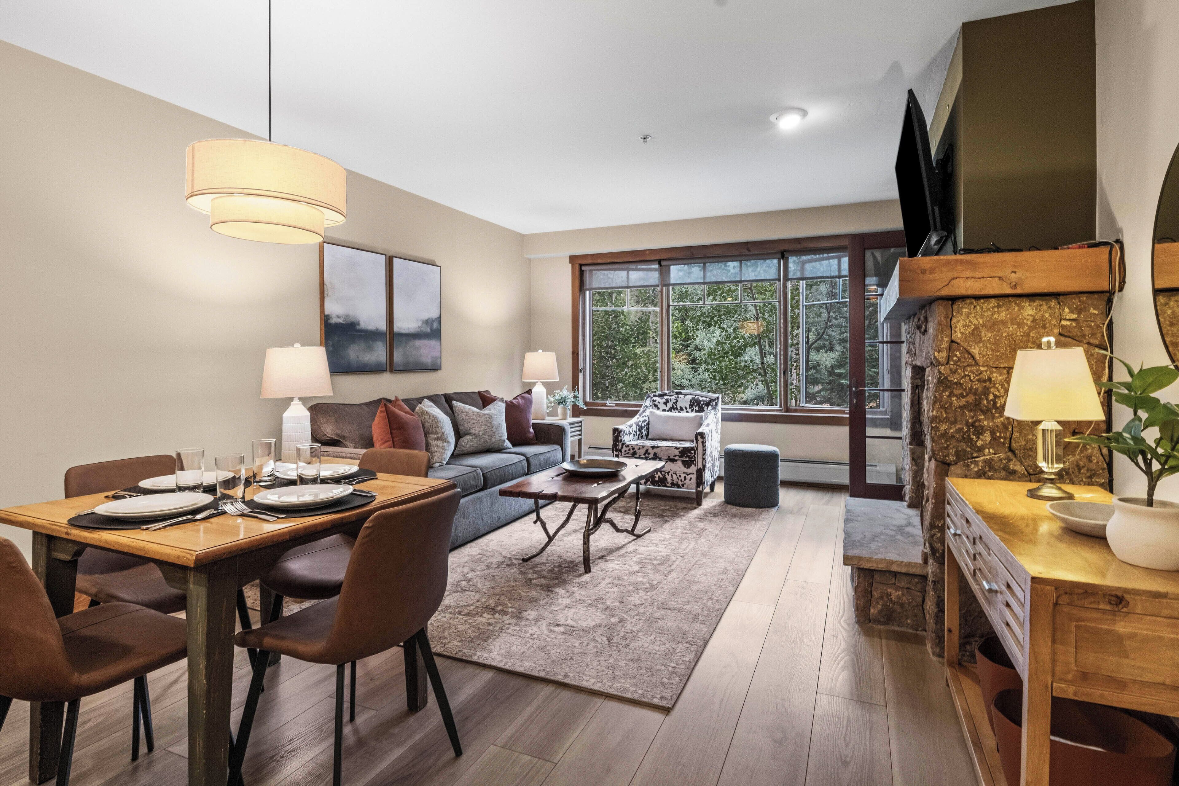 A modern living room with a dining area, a sofa, a coffee table, and a television mounted on the wall.