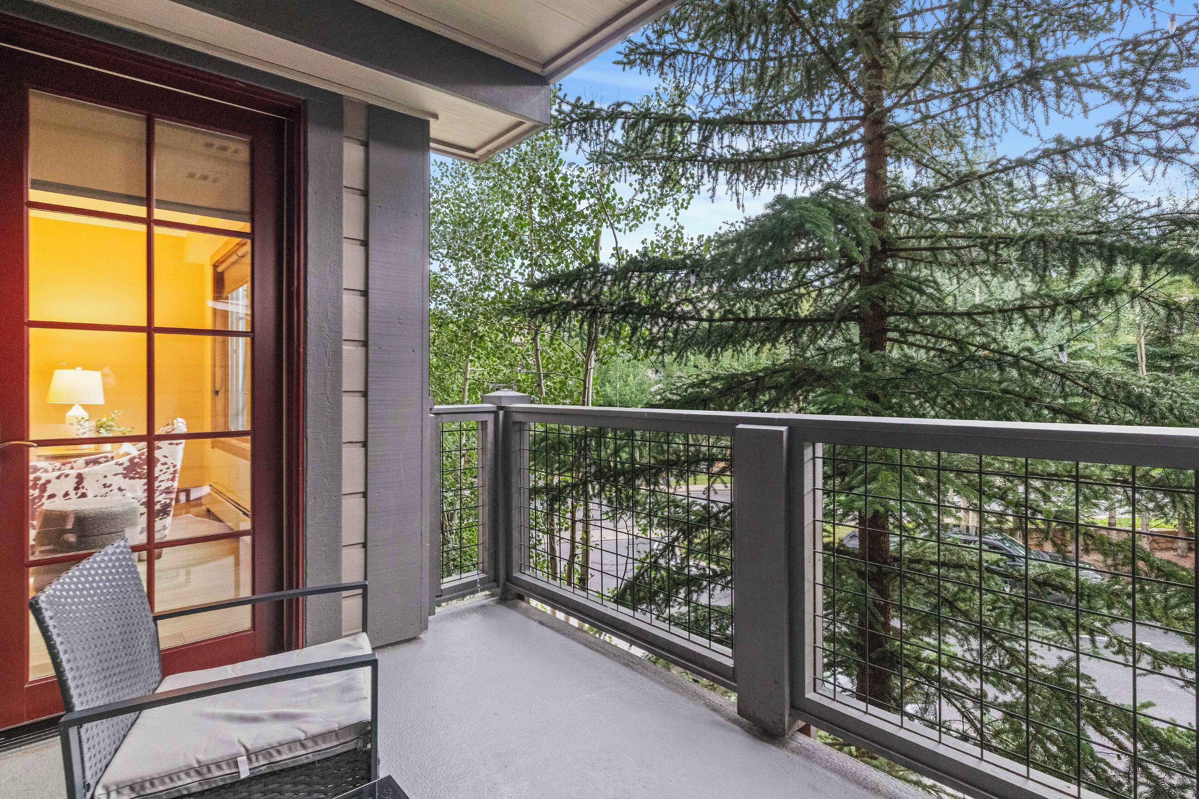 Un balcón con vistas a un bosque, una silla y una ventana con una lámpara en su interior.