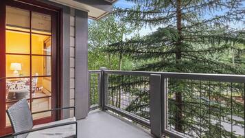 A balcony with a view of a forest, a chair, and a window with a lamp inside.
