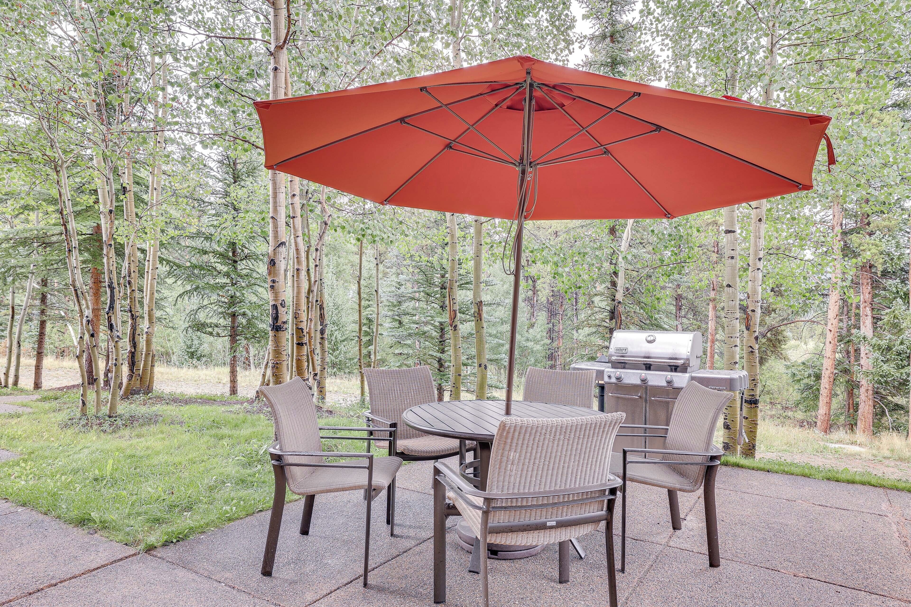 Une terrasse extérieure avec une table et des chaises, un parasol rouge et un barbecue.