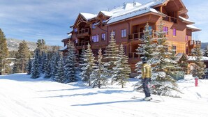 A multi-story wooden lodge with balconies and large windows, surrounded by snow-covered trees.