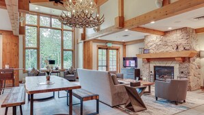 A spacious living area with a stone fireplace, wooden beams, and a large window overlooking a forest.