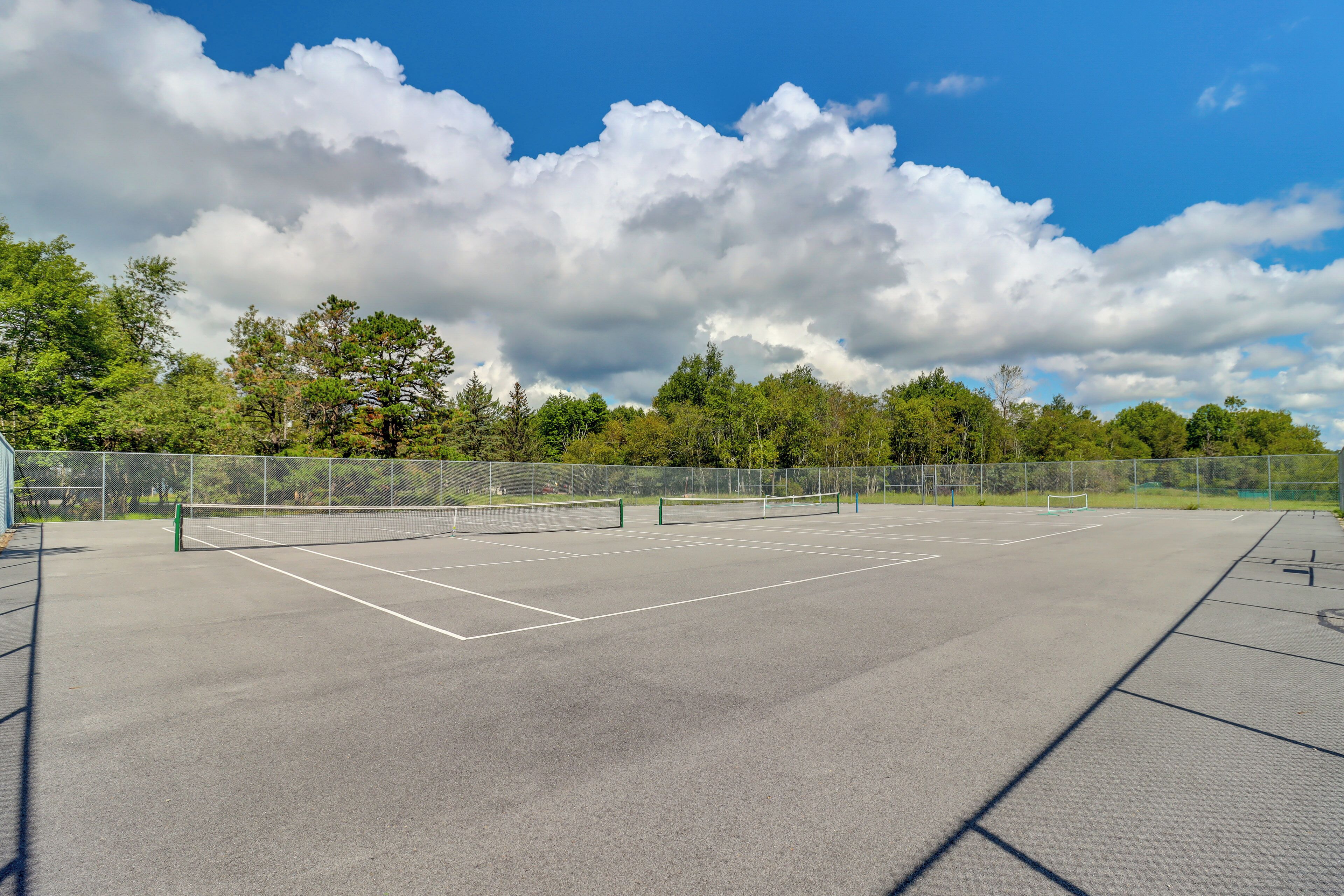 An outdoor tennis court with a net, surrounded by trees and a clear sky.