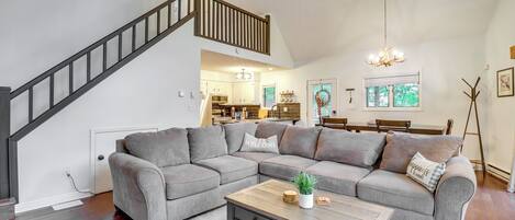 A modern living room with a gray sectional sofa, a wooden coffee table, and a staircase with a wooden railing.