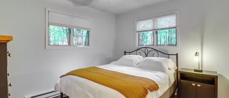 A bedroom with a bed, a ceiling fan, two windows, a nightstand, and a heater.
