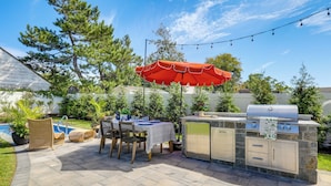 Un patio al aire libre con mesa, sillas, una parrilla y una piscina.