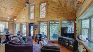 Une cabane en bois spacieuse, dotée d’un plafond haut, d’une cheminée, d’une télévision et d’un coin repas.