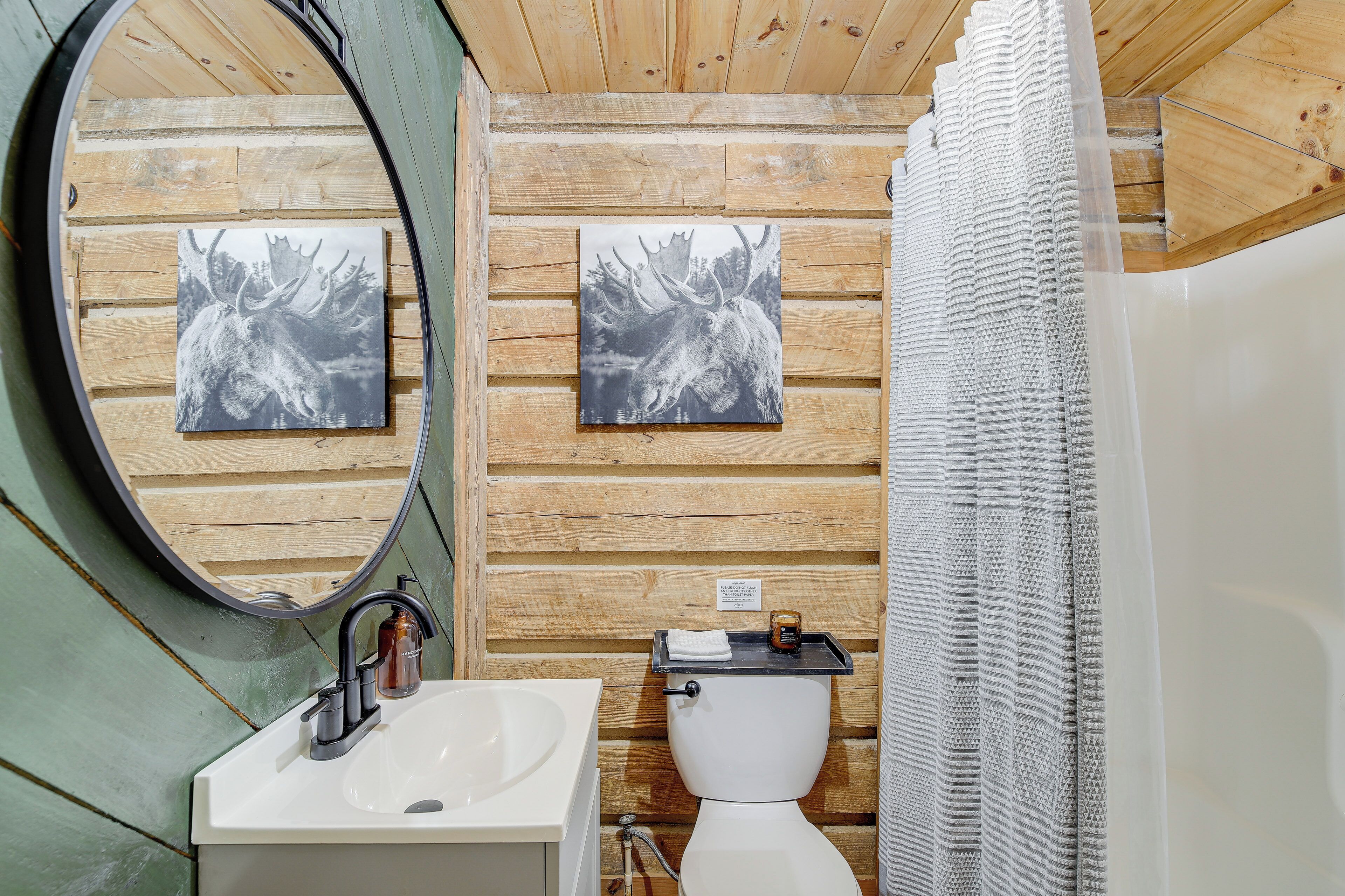 Un baño con paredes de madera, un lavamanos blanco, un espejo y dos cuadros de alces.