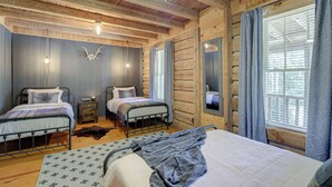 Een slaapkamer in een blokhut met twee bedden, een groot raam met gordijnen, houten wanden en een plafondventilator.