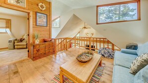 A spacious living area with wooden flooring, a wooden coffee table, a blue sofa, and a staircase with a wooden railing. - Ruidoso Cabin w/ Deck + Views: 4 Mi to Winter Park (Ruidoso)