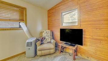 A cozy living room with a wooden wall, a large TV, a beige sofa, and a standing heater.