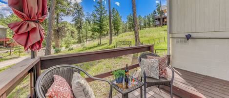 A wooden deck with wicker chairs and a table, overlooking a grassy area with trees.
