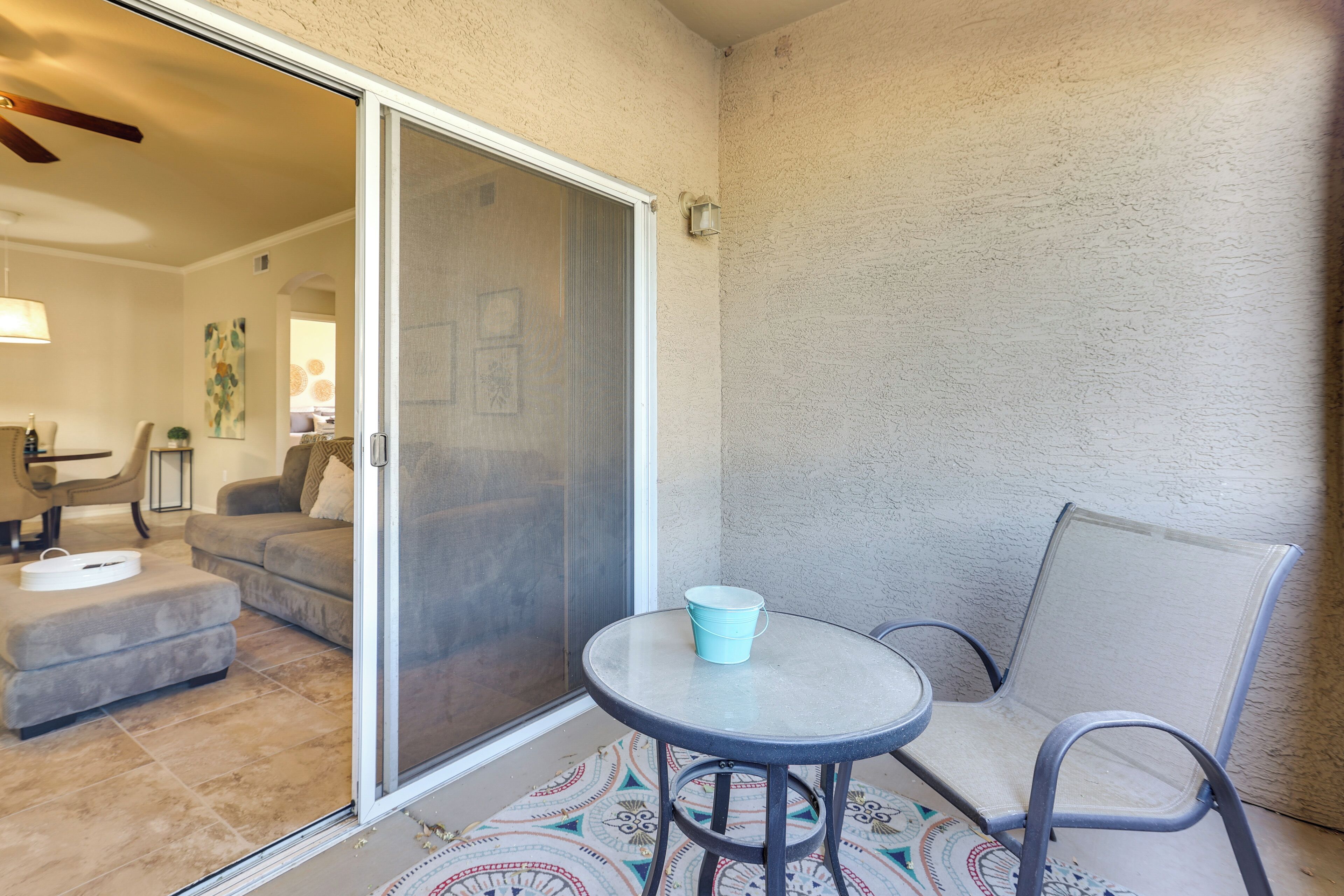 A patio area with a sliding glass door leading to a living room, a round table with a chair, and a patterned rug.