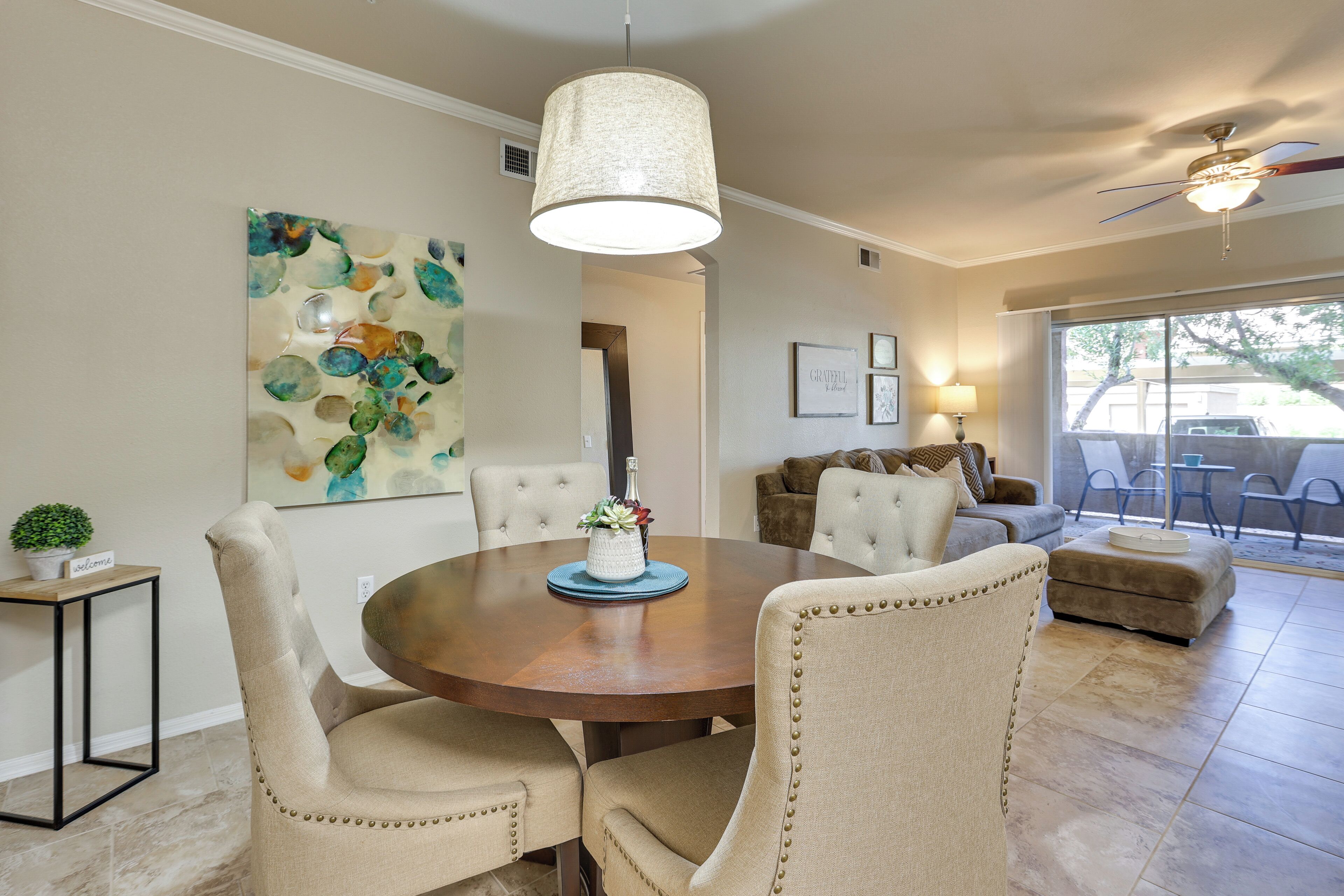 A dining area with a round table, beige upholstered chairs, and a hanging light fixture.
