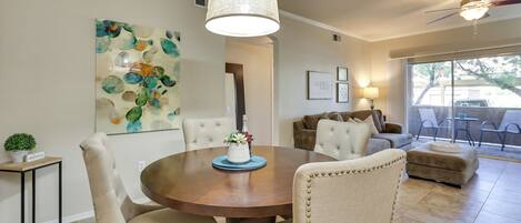 A dining area with a round table, beige upholstered chairs, and a hanging light fixture.