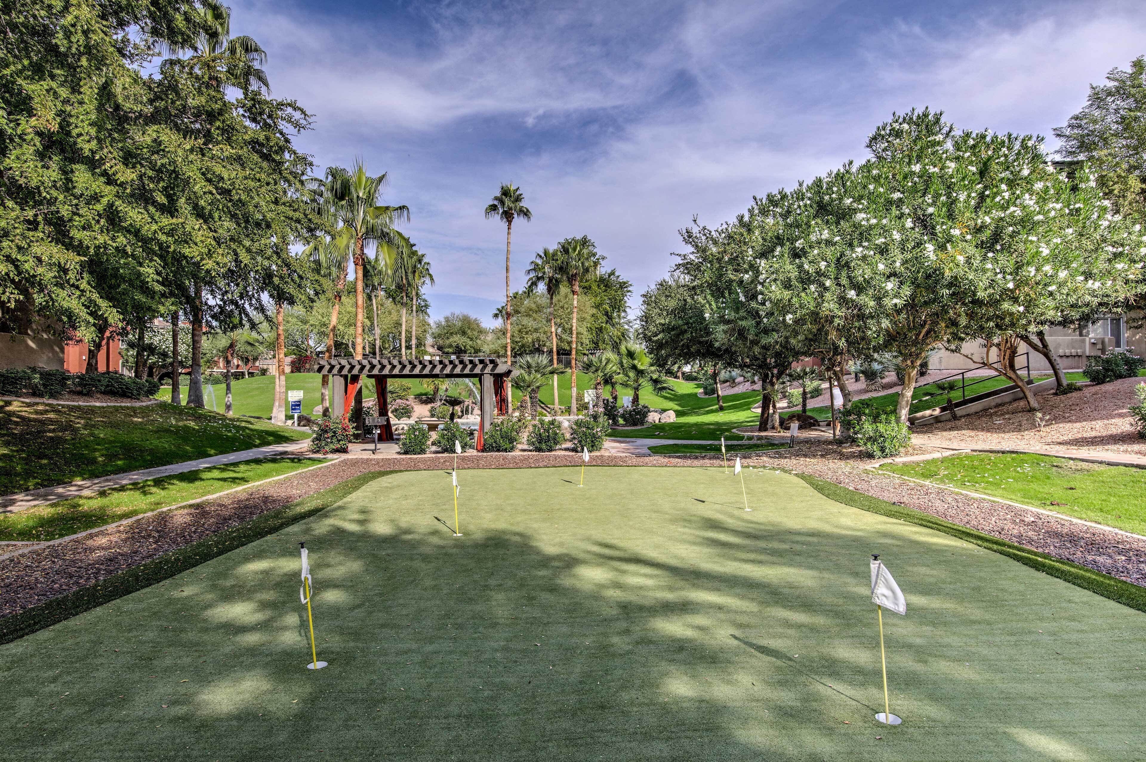 Un campo de golf con un césped de práctica bien cuidado, rodeado de exuberante follaje y palmeras.