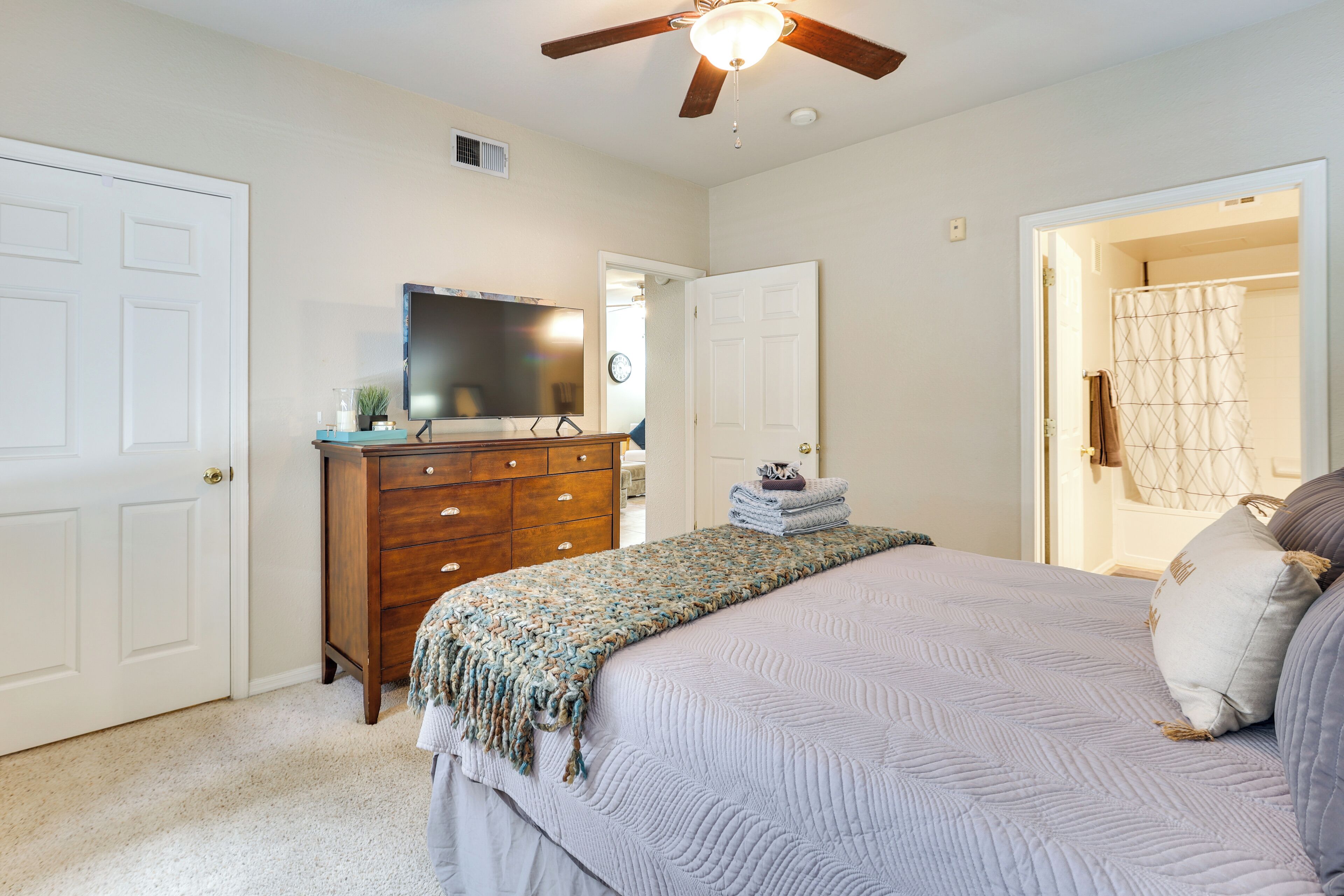 A bedroom with a bed, dresser, television, and a ceiling fan.