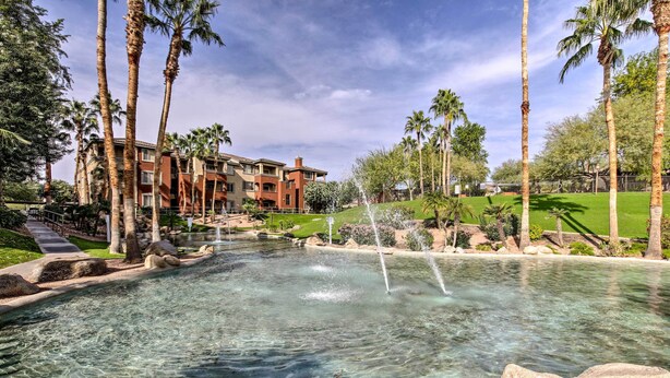 A clear pool with a fountain, surrounded by palm trees and a building with multiple balconies. - Walk to Papago Park: Central Phoenix Condo (Phoenix)
