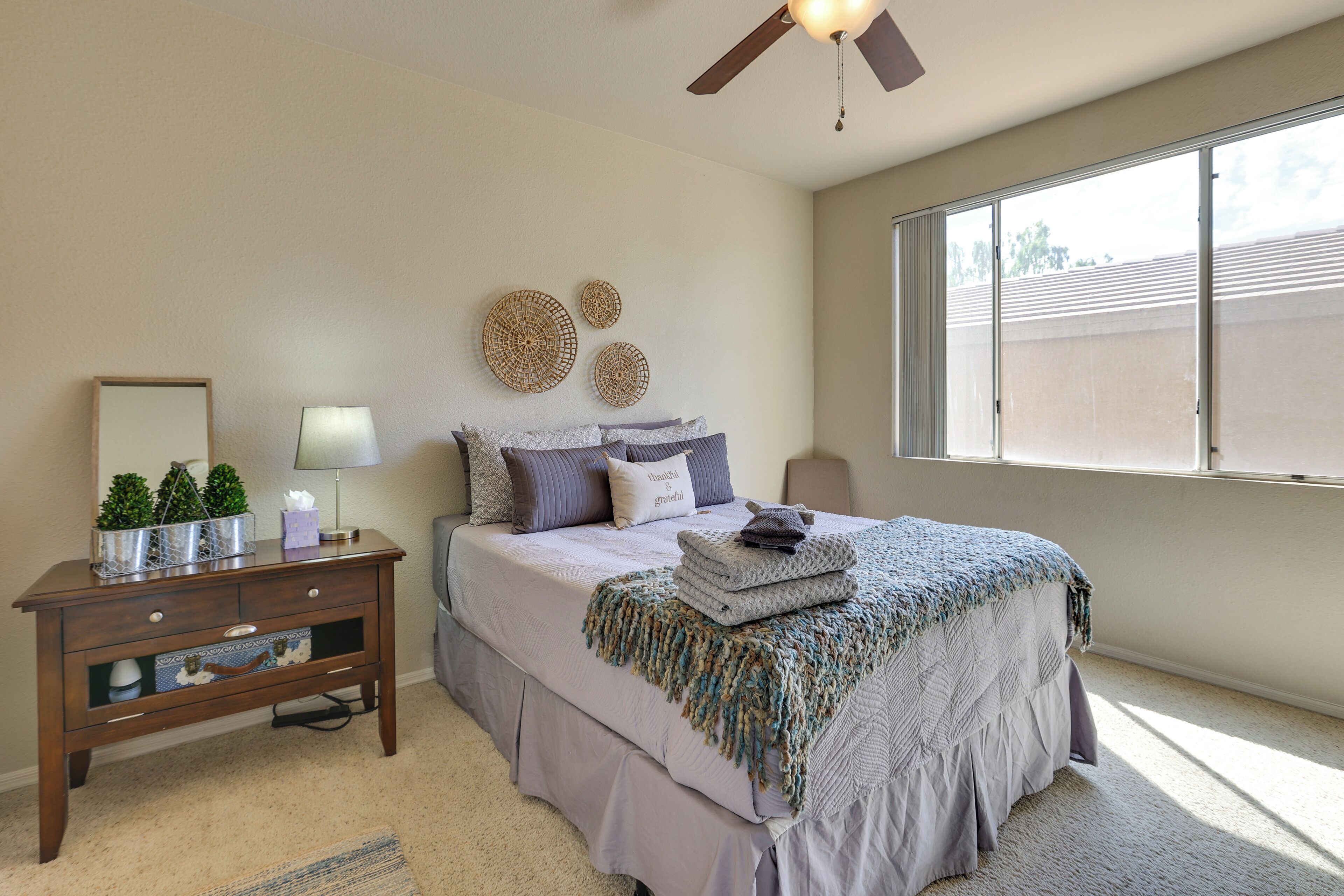 A bedroom with a bed, bedside table, lamp, decorative wall art, and a window with blinds.