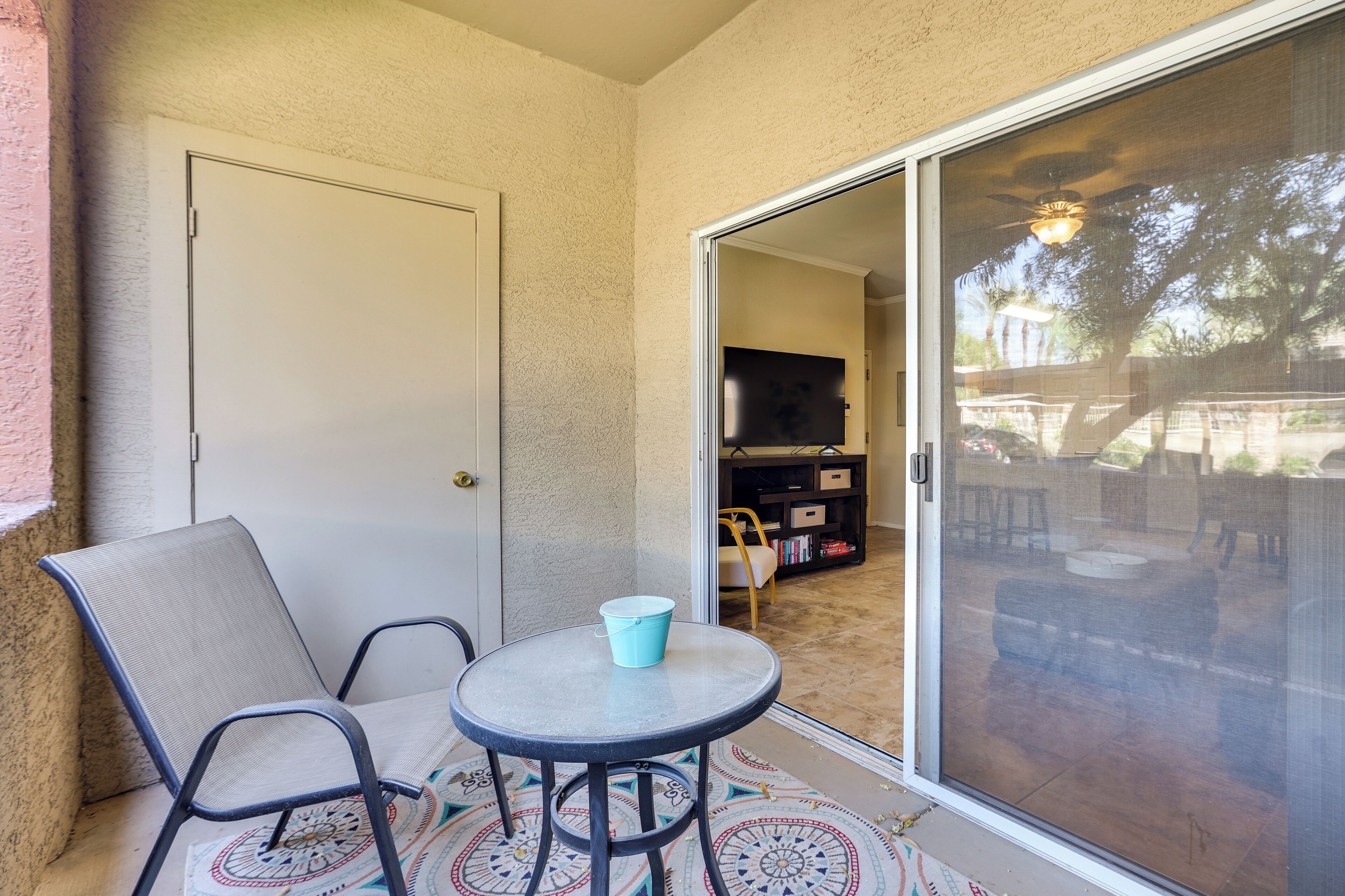 A small balcony with a sliding glass door, a round table with a blue bucket, and a chair.
