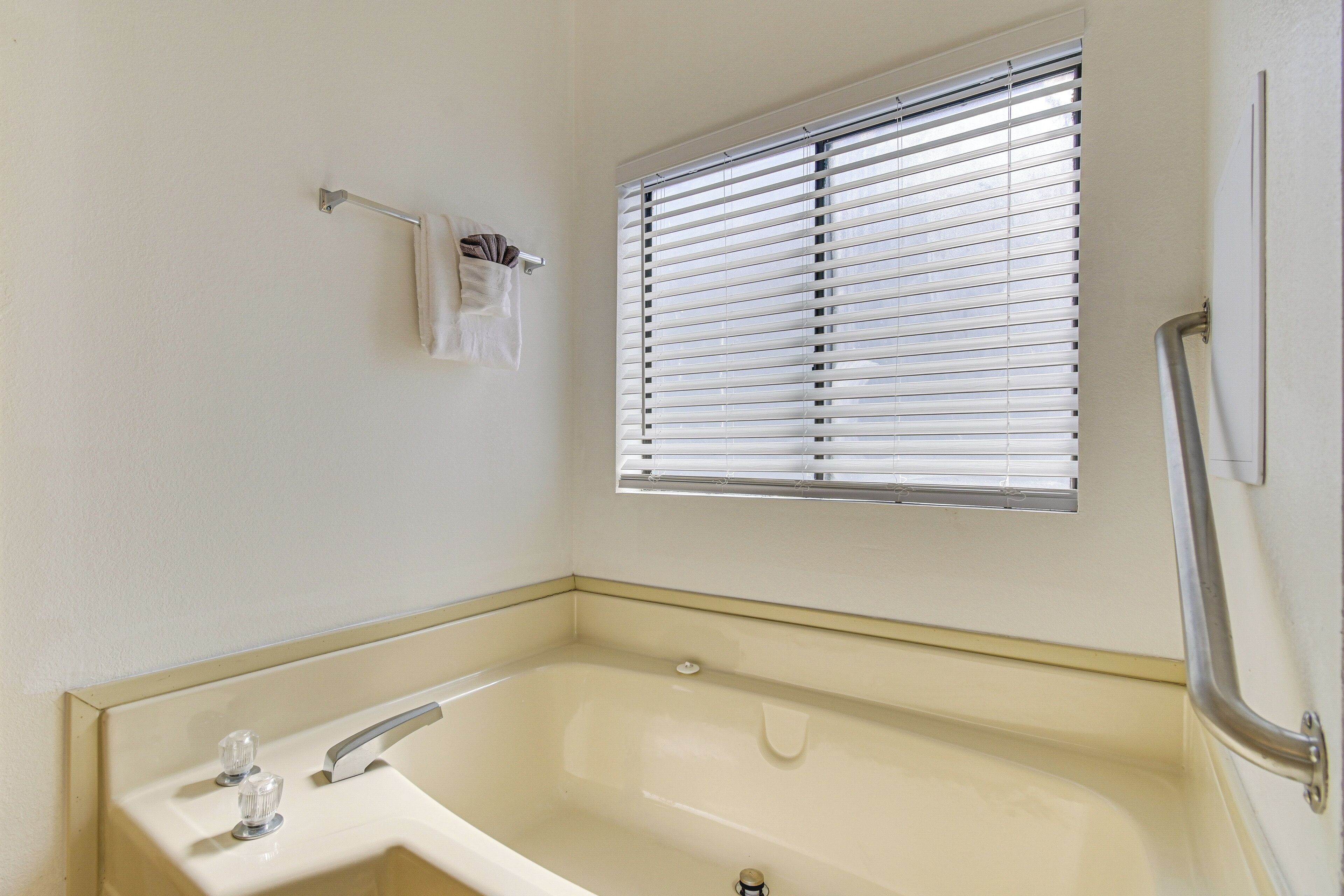 Un baño con bañera, una ventana con persianas y un perchero.