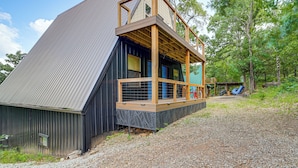 A two-story building with a wooden deck and a metal railing. - Lake Eufaula Cabin w/ Hot Tub & Large Deck (Stigler)