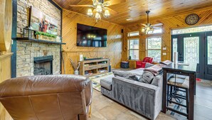 A wooden interior with a fireplace, a sofa, a television, and a dining area. - Lake Eufaula Cabin w/ Hot Tub & Large Deck (Stigler)