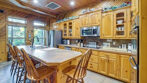 A kitchen with wooden cabinets, a large island with bar stools, a refrigerator, and a microwave. - Lake Eufaula Cabin w/ Hot Tub & Large Deck (Stigler)