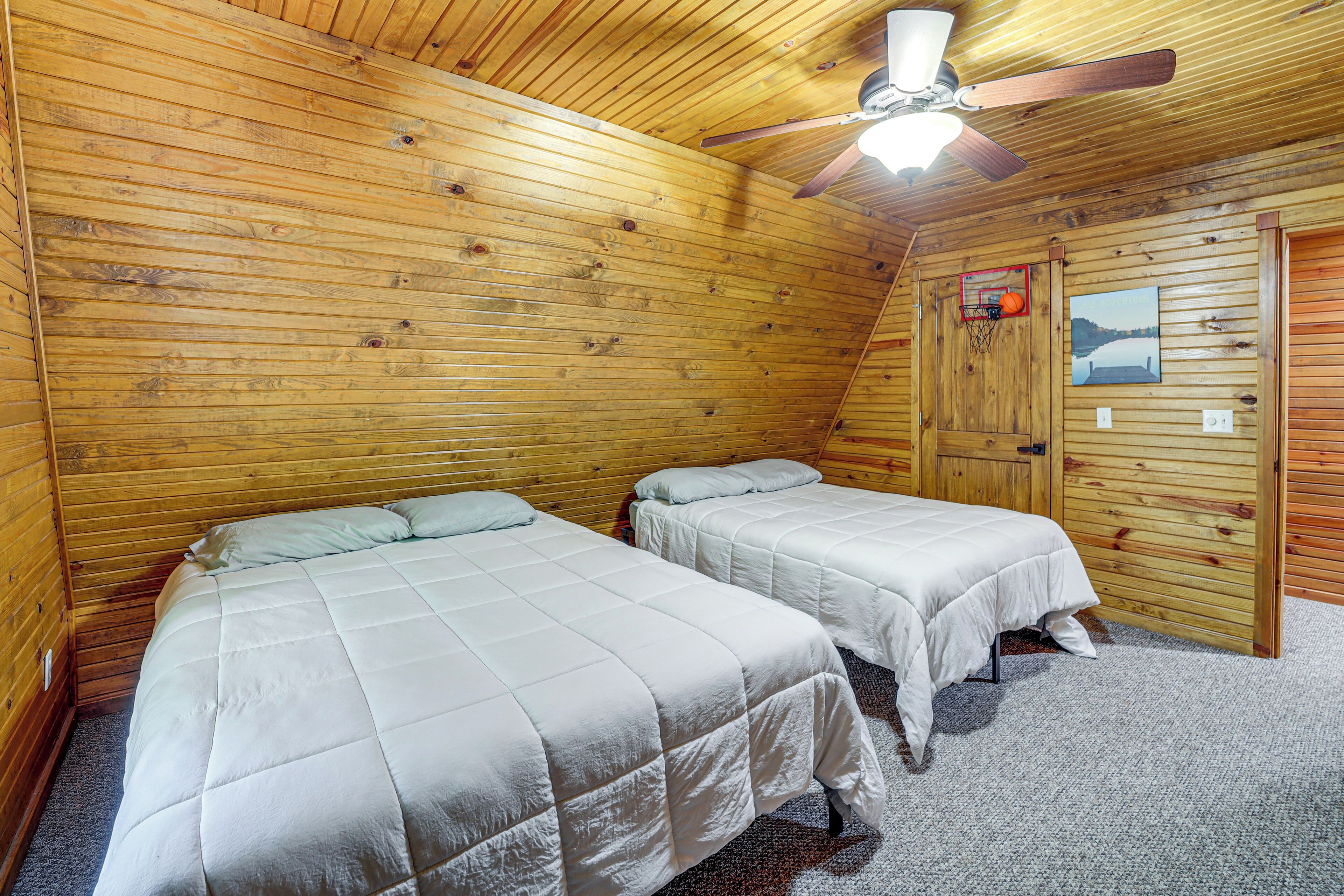 A room with two beds, a ceiling fan, and a door with a picture.
