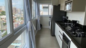 A modern kitchen with large windows, a refrigerator, stove, and a microwave. - Dallas Apartamentos (Bento Gonçalves)