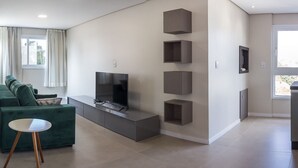 A modern living room with a flat-screen TV, a green sofa, and built-in shelving. - Dallas Apartamentos (Bento Gonçalves)