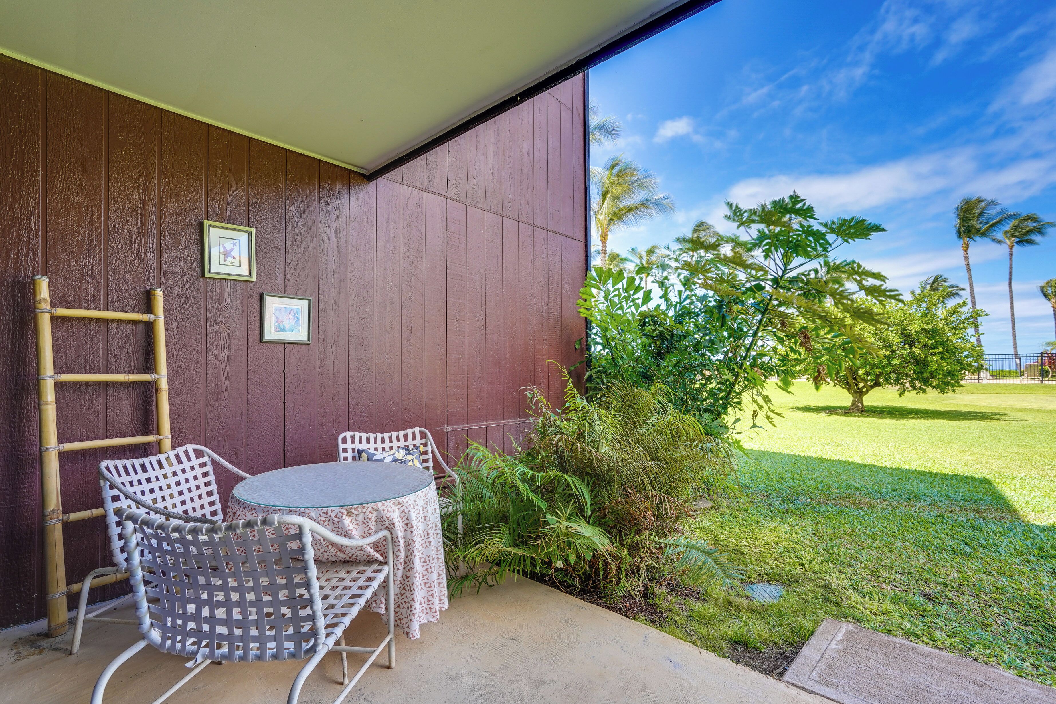 A patio with a table and chairs, a wooden ladder, and a view of a grassy area with trees.