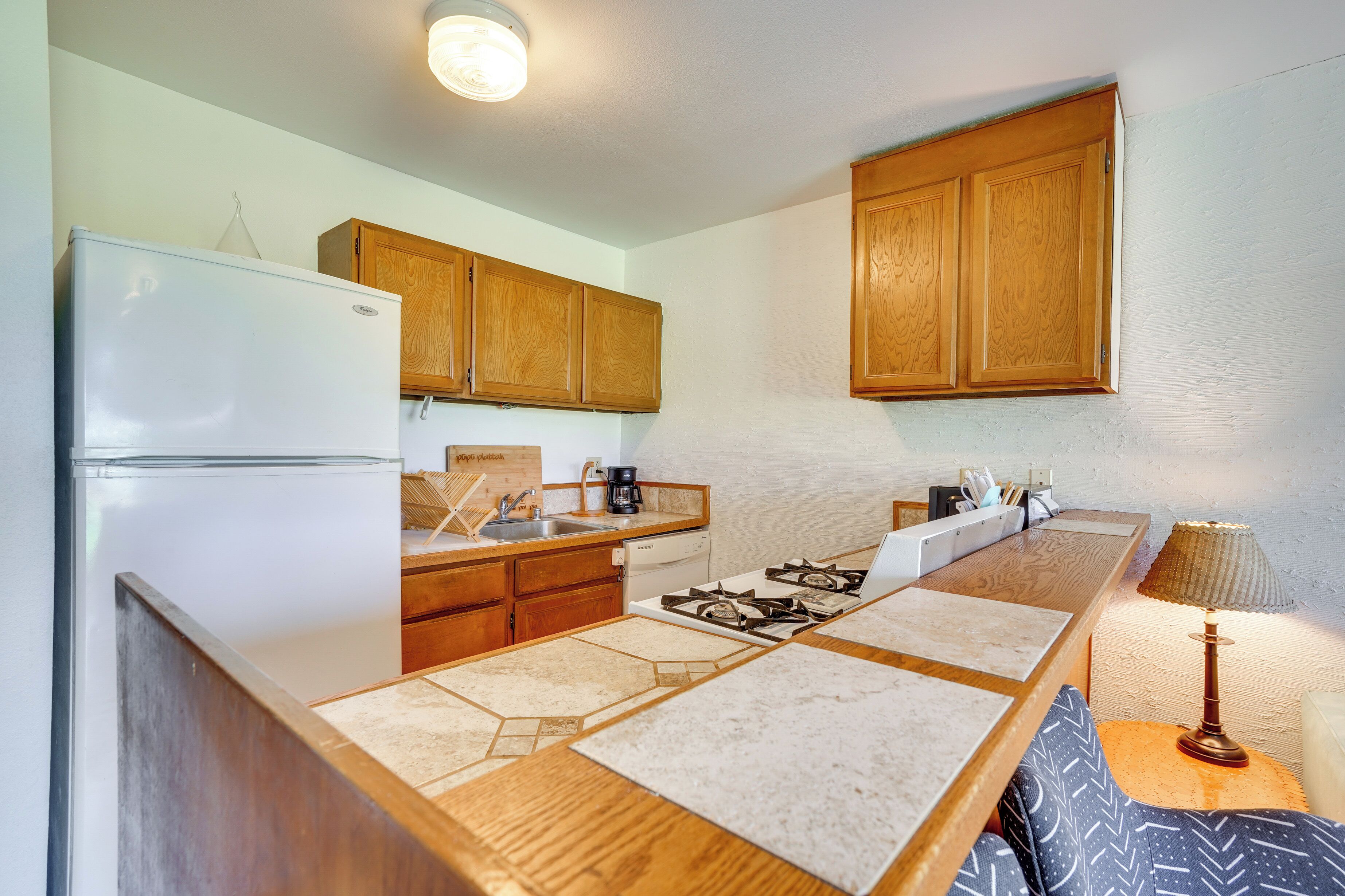 A compact kitchen with wooden cabinets, a white refrigerator, a stove, and a sink.