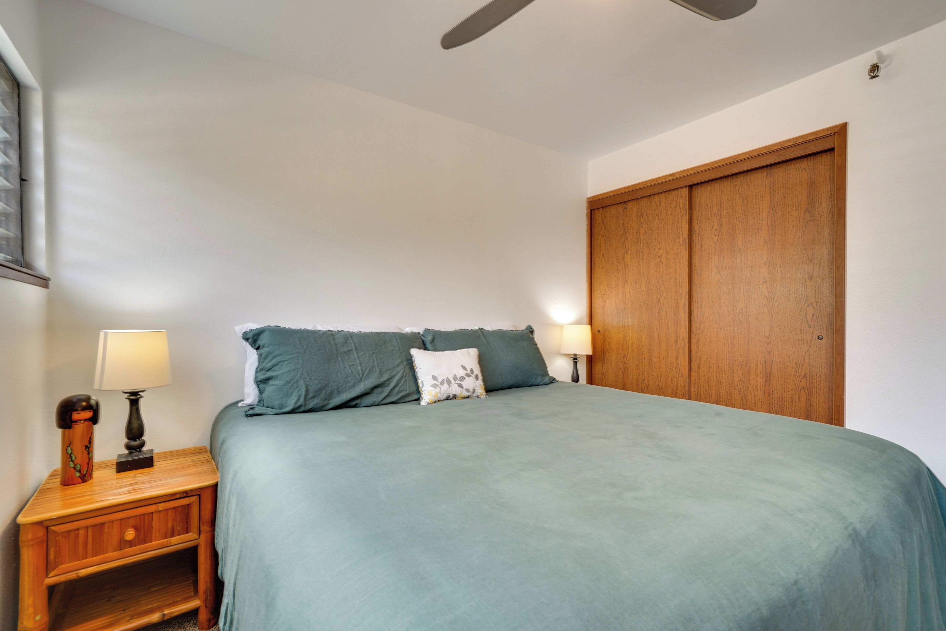 Een slaapkamer met een bed, nachtkastjes, een houten garderobe en een plafondventilator.