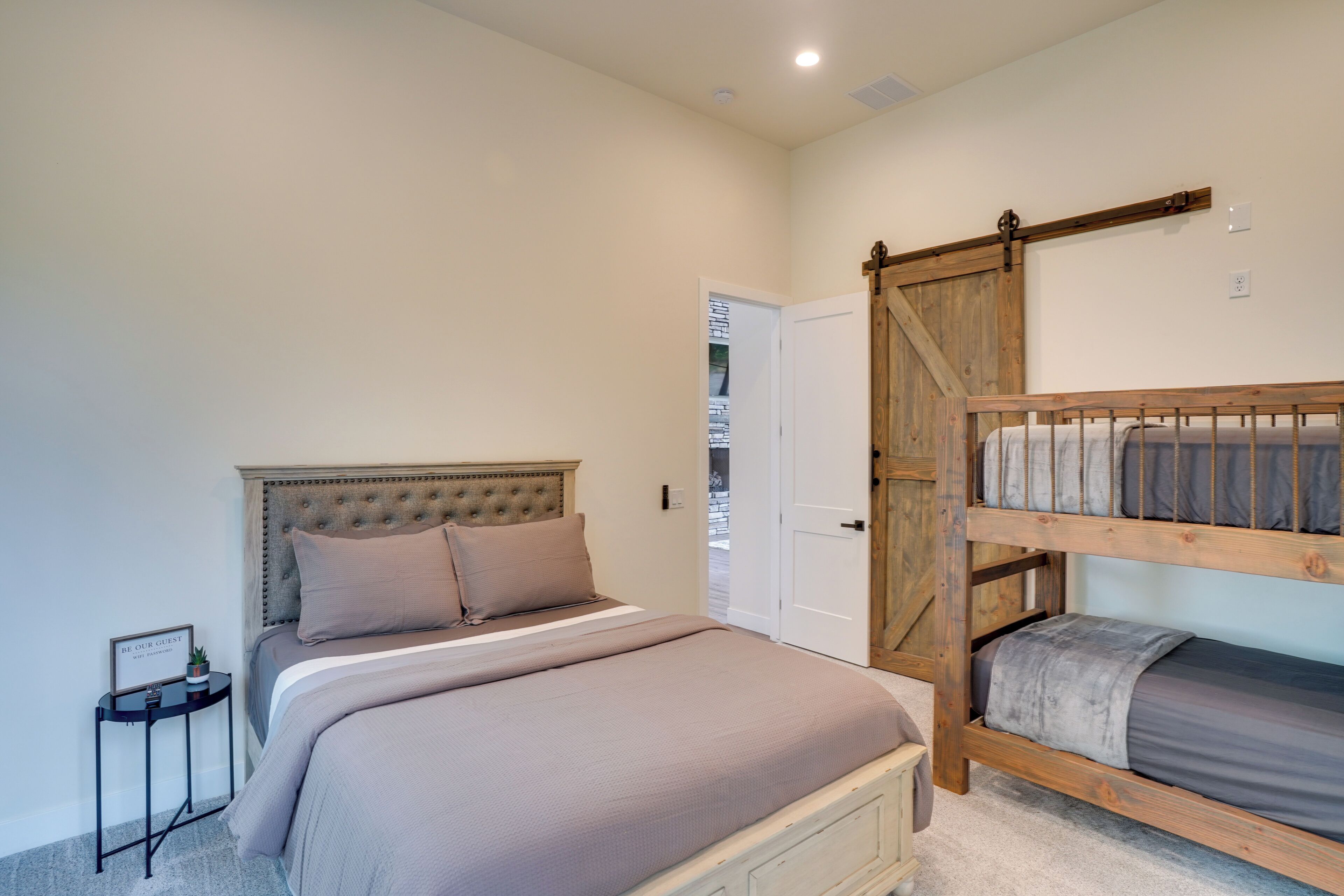 A bedroom with a large bed, a smaller bed on a platform, a bedside table with a plant, and a door leading to a balcony.