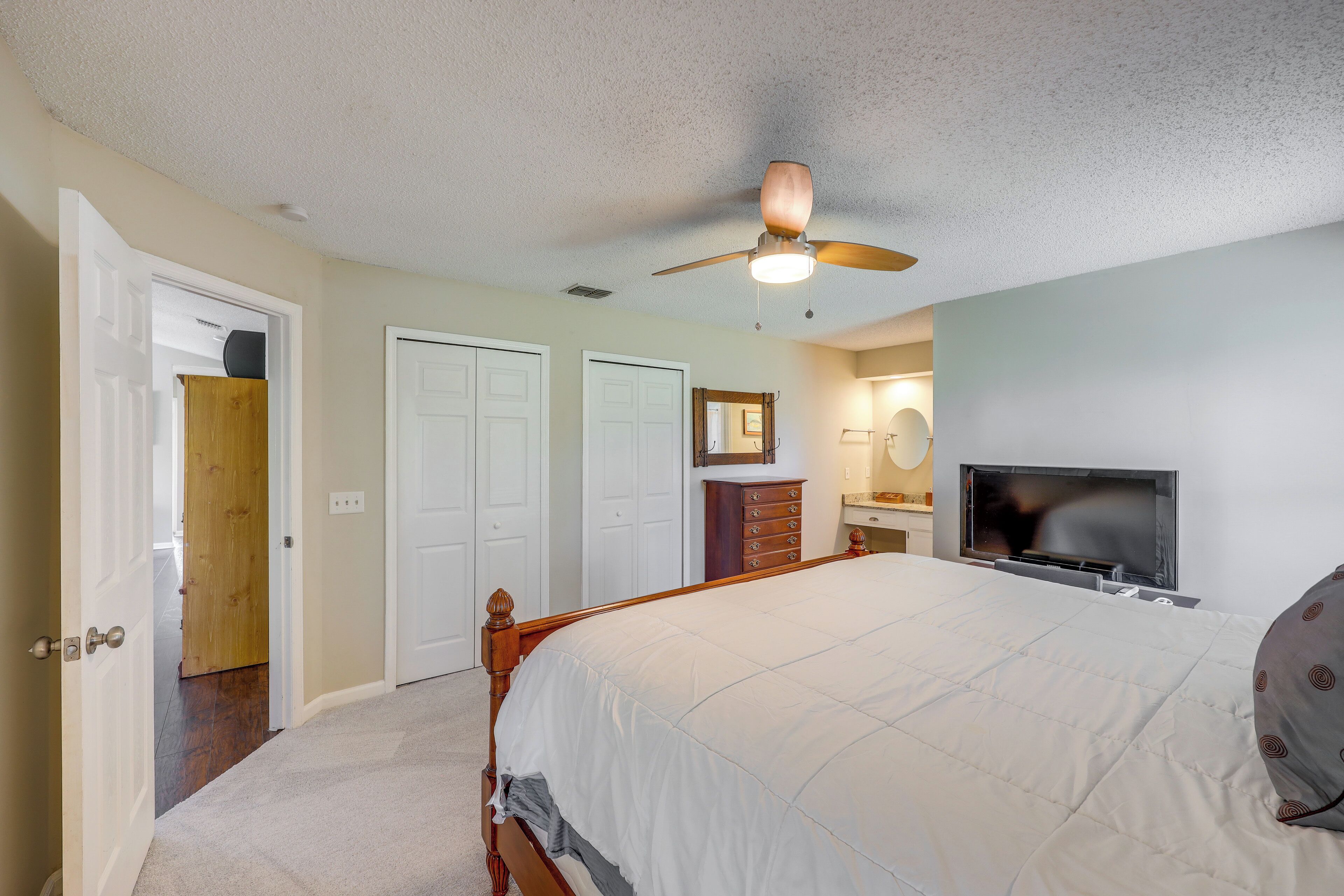 A bedroom with a bed, a ceiling fan, a TV, and a dresser.