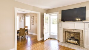 A spacious living room with hardwood flooring, a fireplace, a television mounted above it, and a dining area with chairs and a table. - Charming Tullahoma Stay w/ Great Walkable Location (Tullahoma)