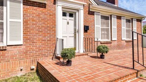 A brick house with a white front door, white shutters, and a small front porch with two potted plants. - Charming Tullahoma Stay w/ Great Walkable Location (Tullahoma)