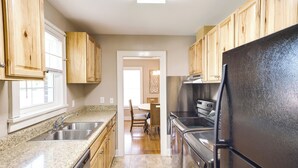 A kitchen with wooden cabinets, a black refrigerator, stainless steel appliances, granite countertops, and a dining area with a table and chairs. - Charming Tullahoma Stay w/ Great Walkable Location (Tullahoma)