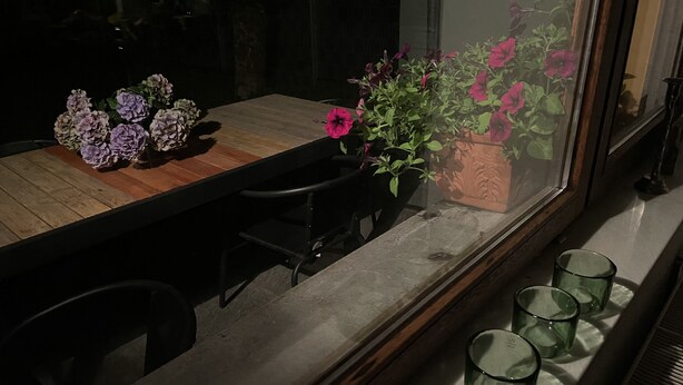 A dining table with a wooden top, surrounded by chairs, and a window with a view of flowers and a building. - Behagliches Haus mit Kamin (Monschau)