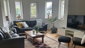A living room with a black leather sofa, a wooden coffee table, a patterned rug, and a television. - Behagliches Haus mit Kamin (Monschau)