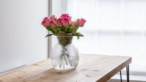 Ein Holztisch mit einer klaren Glasvase, die rosa Rosen enthält.