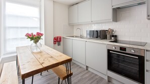 Eine moderne Küche mit weißen Schränken, einer Edelstahl-Mikrowelle, einem eingebauten Backofen und einem Holztisch mit Blumen in einer Vase.