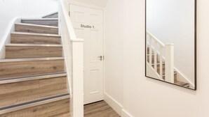 Eine Treppe mit hölzernen Stufen und weißen Geländern, die zu einer Tür führt, auf der „Studio 1“ steht.