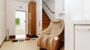 A massage chair in a room with a wooden staircase, a door with an emergency exit sign, and a small white cabinet.
