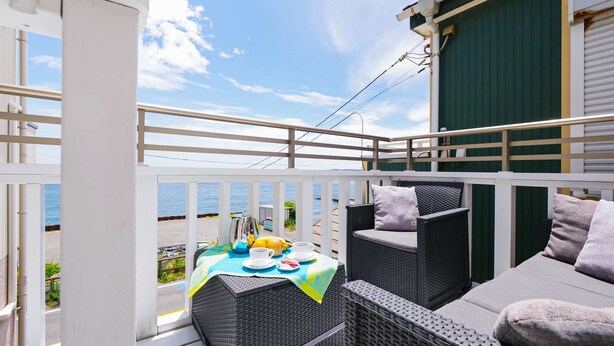 A balcony with wicker furniture, a table with a placemat, and a view of the sea.
