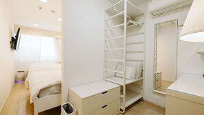 A bedroom with a bed, a wardrobe, a desk, a trash bin, and a mirror.