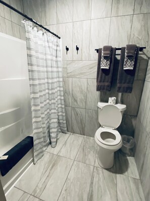 Un baño con un inodoro blanco, una cortina de ducha a rayas y un perchero con dos toallas.